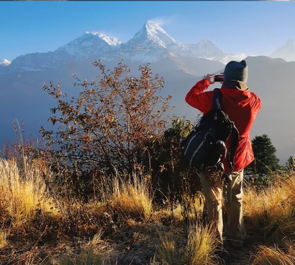 Elevate Trek- A man in a red jacket and backpack clicking the picture of scenic snow-capped Annapurna Massif