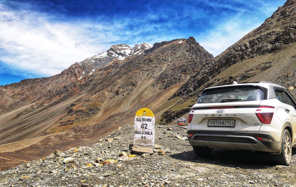A white SUV on a rugged mountain road with a distance marker in the Himalayas.