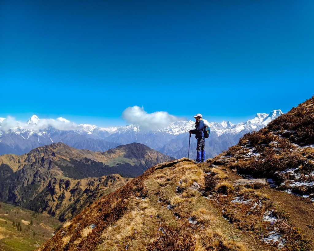A hiker enjoys breathtaking views of the Himalayan mountain range under a clear blue sky.
