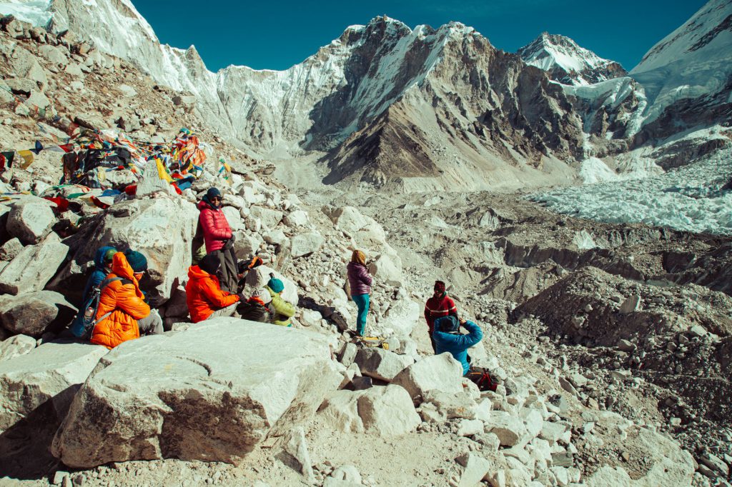 Group of trekkers resting at Everest Base Camp surrounded by prayer flags and snowy peaks in the Himalayas.