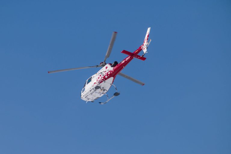 A vibrant red and white helicopter in flight against a clear blue sky, showcasing aviation dynamics.