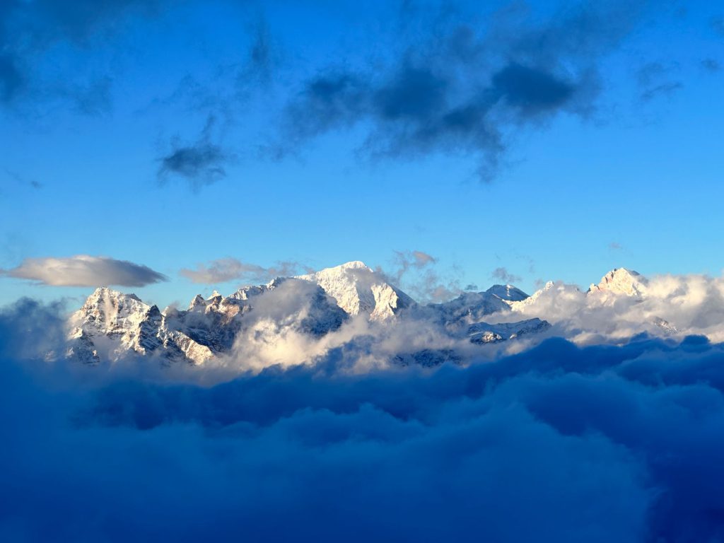 Stunning view of snow-covered mountains rising through fluffy clouds under a vibrant blue sky.