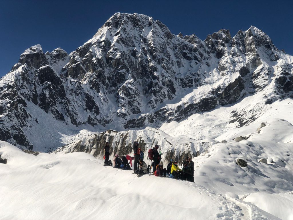 Group of climbers ascending snowy Himalayan peak under bright blue sky.