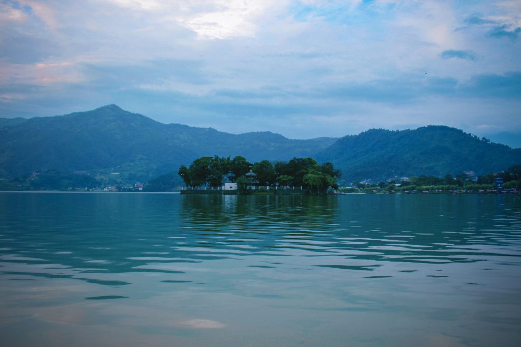 Serene view of Fewa Lake with surrounding mountains in Pokhara, Nepal, under a cloudy sky.