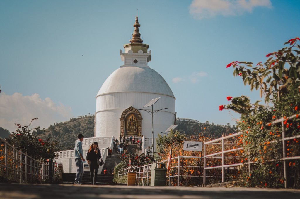 Tourists walking near the World Peace Pagoda surrounded by flowers in Nepal.