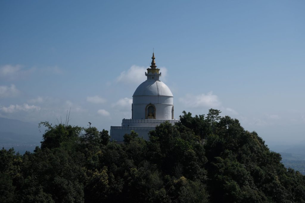 Serene white pagoda atop a lush forested hill under a clear blue sky, representing architectural beauty.