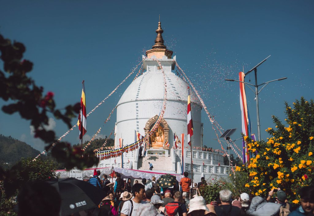 Spectacular festival at World Peace Pagoda with vibrant flags and large crowd in Pokhara, Nepal.