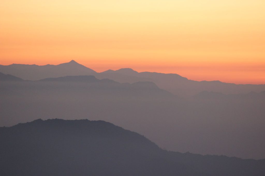 Gentle silhouettes of mountains against a vibrant orange sunrise sky.