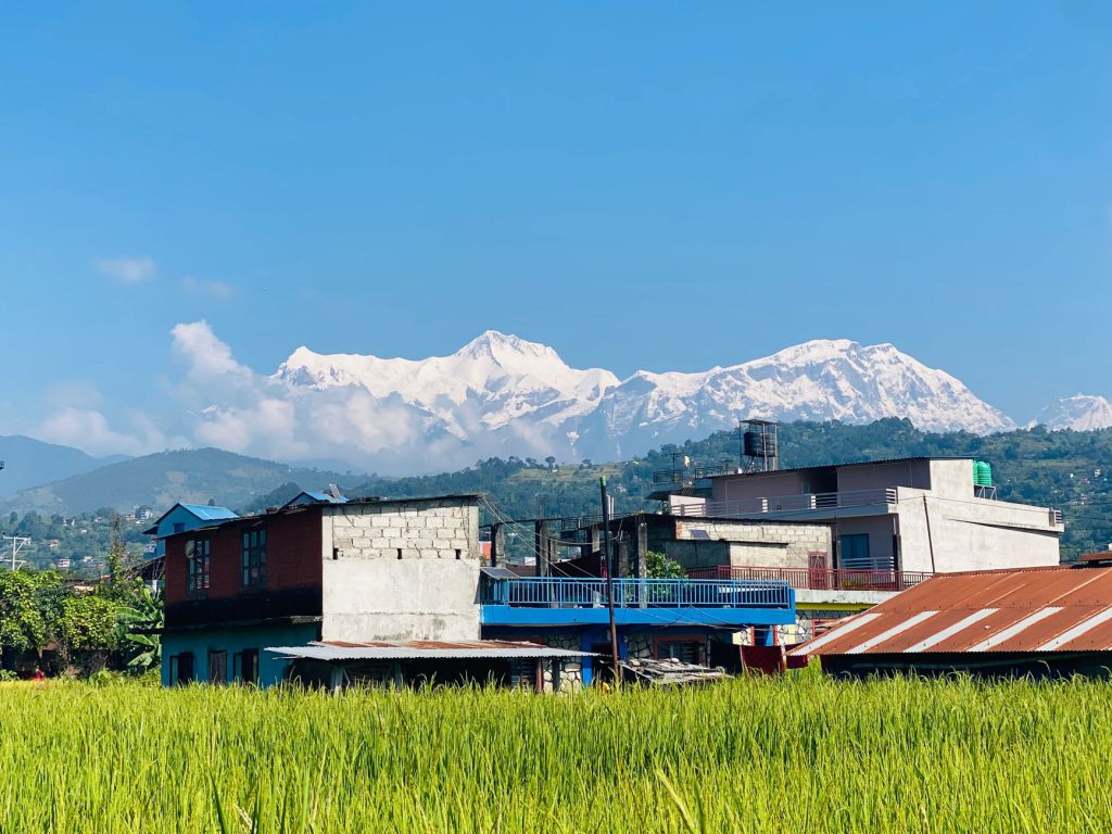 Charming rural village foregrounded by stunning snowy mountain range under blue skies.