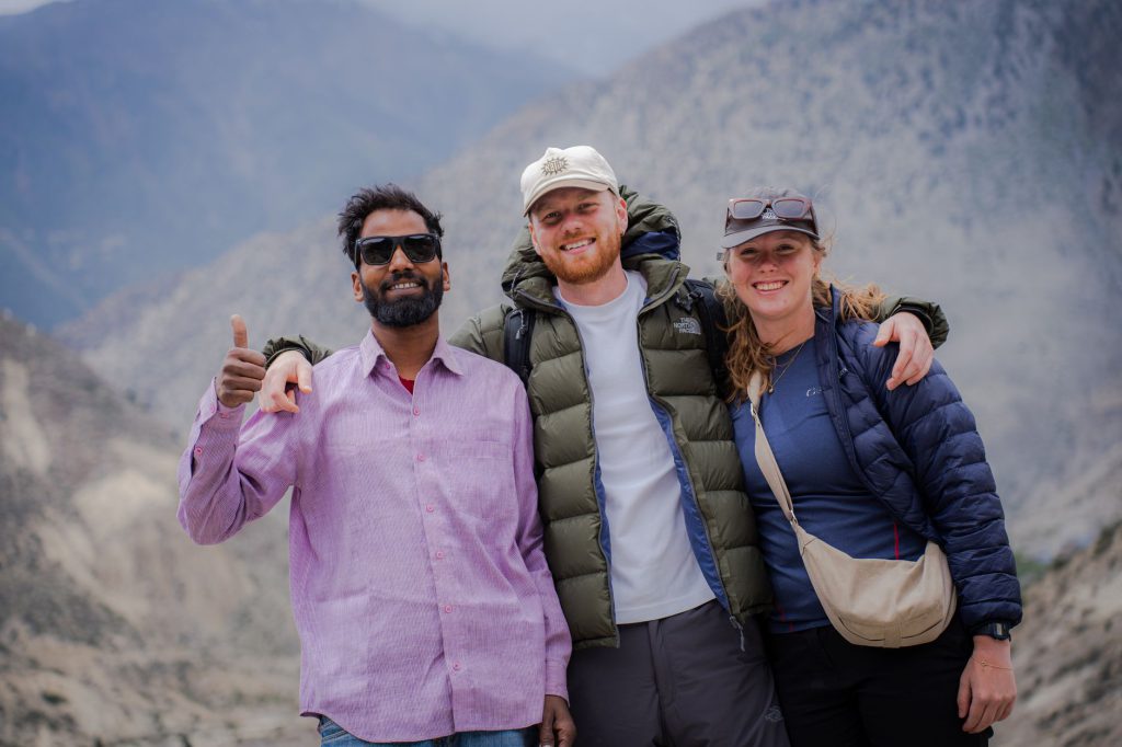 Three friends enjoying a scenic view in Lo Manthang, Nepal, with a mountainous backdrop.