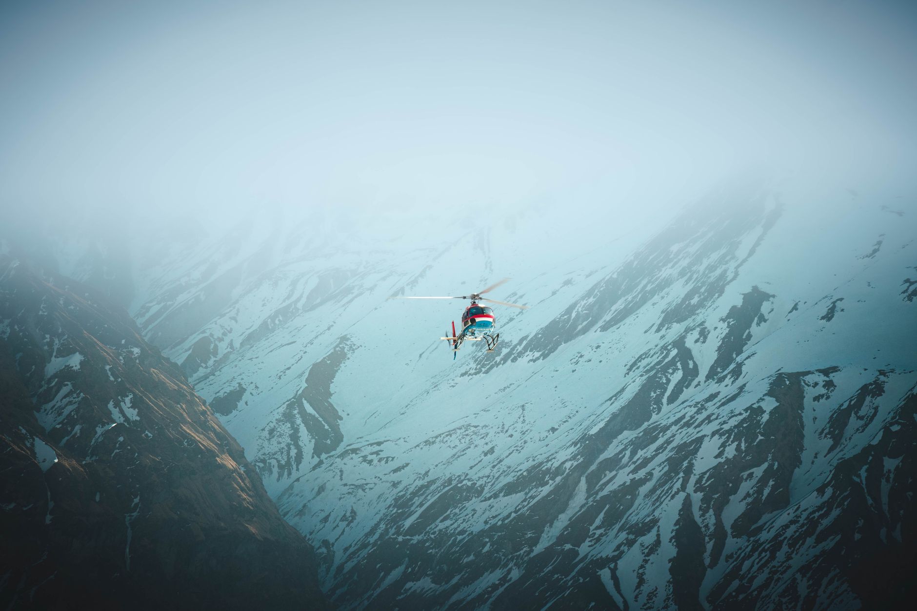 A breathtaking view of a helicopter flying over the snow-covered Himalayan mountains, shrouded in fog.