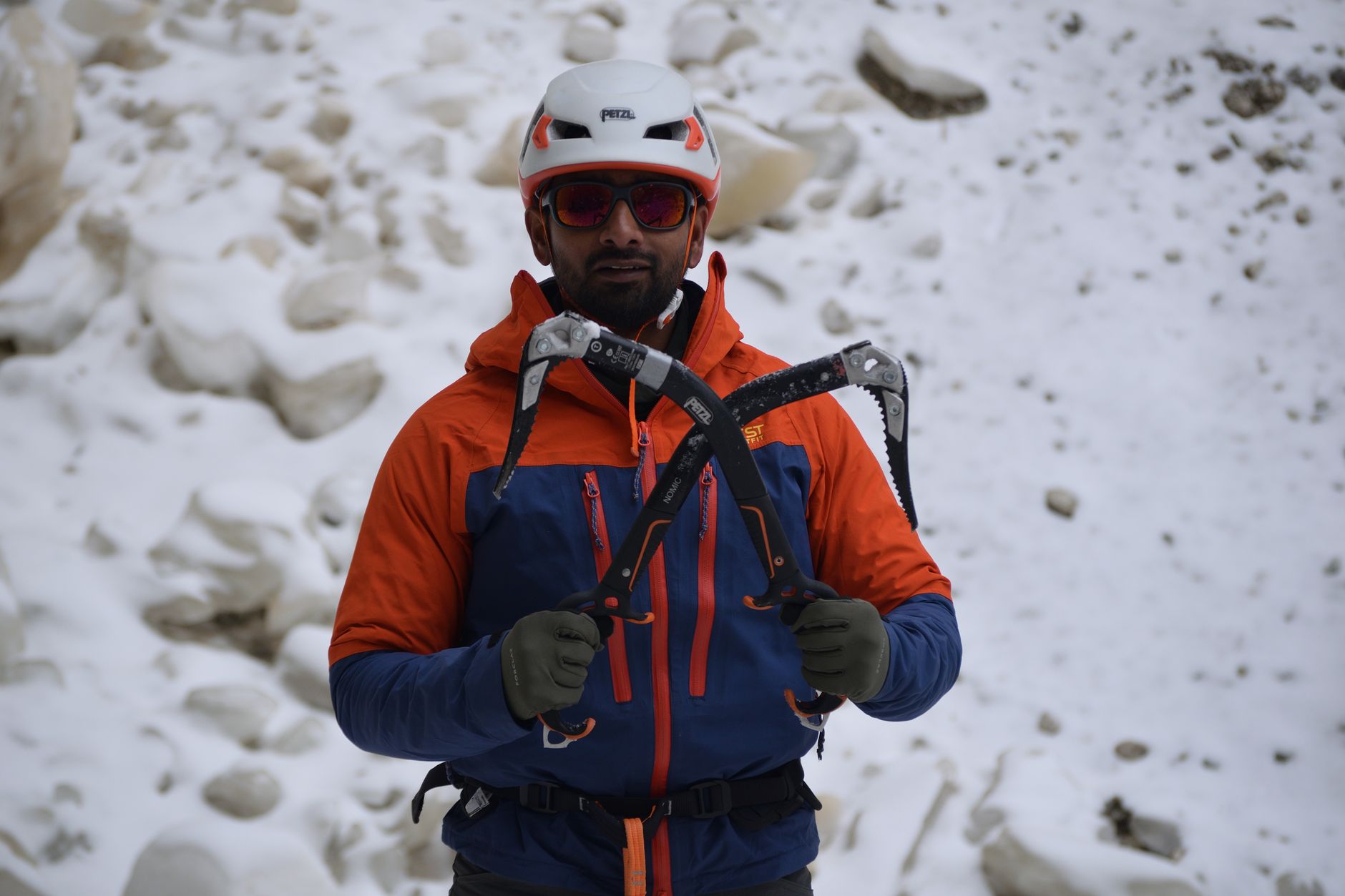 Adult male climber holding ice axes wearing safety gear in a snow-covered landscape.