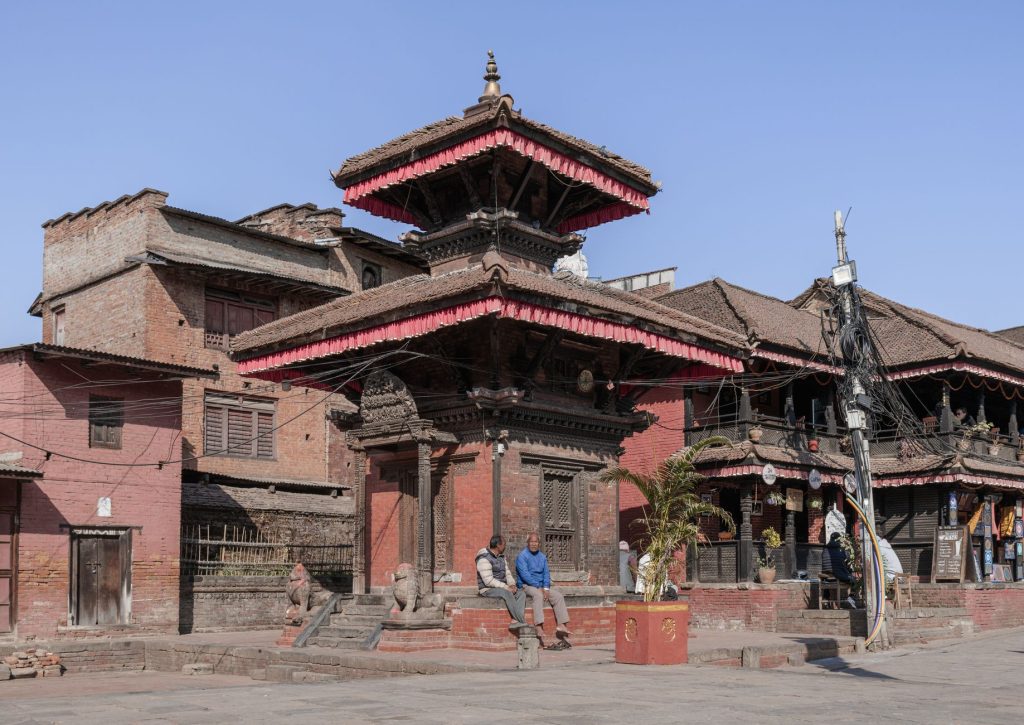 Traditional Nepalese architecture in Bhaktapur's historic Durbar Square with locals relaxing.