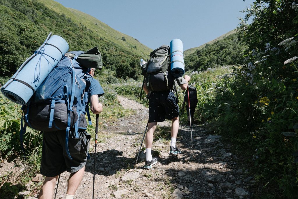 Two backpackers ascending a sunny, rocky mountain path with trekking poles in hand.