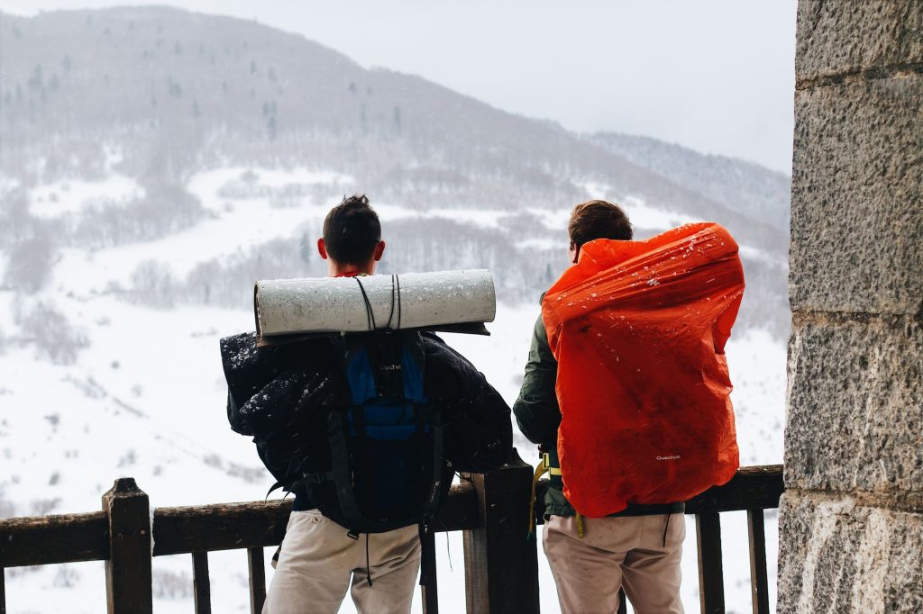 Two male hikers with backpacks enjoying a snowy mountain view in winter.