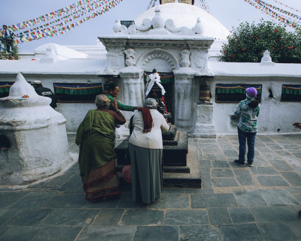 Women participating in a cultural ritual at a historic Buddhist stupa, adorned with prayer flags.